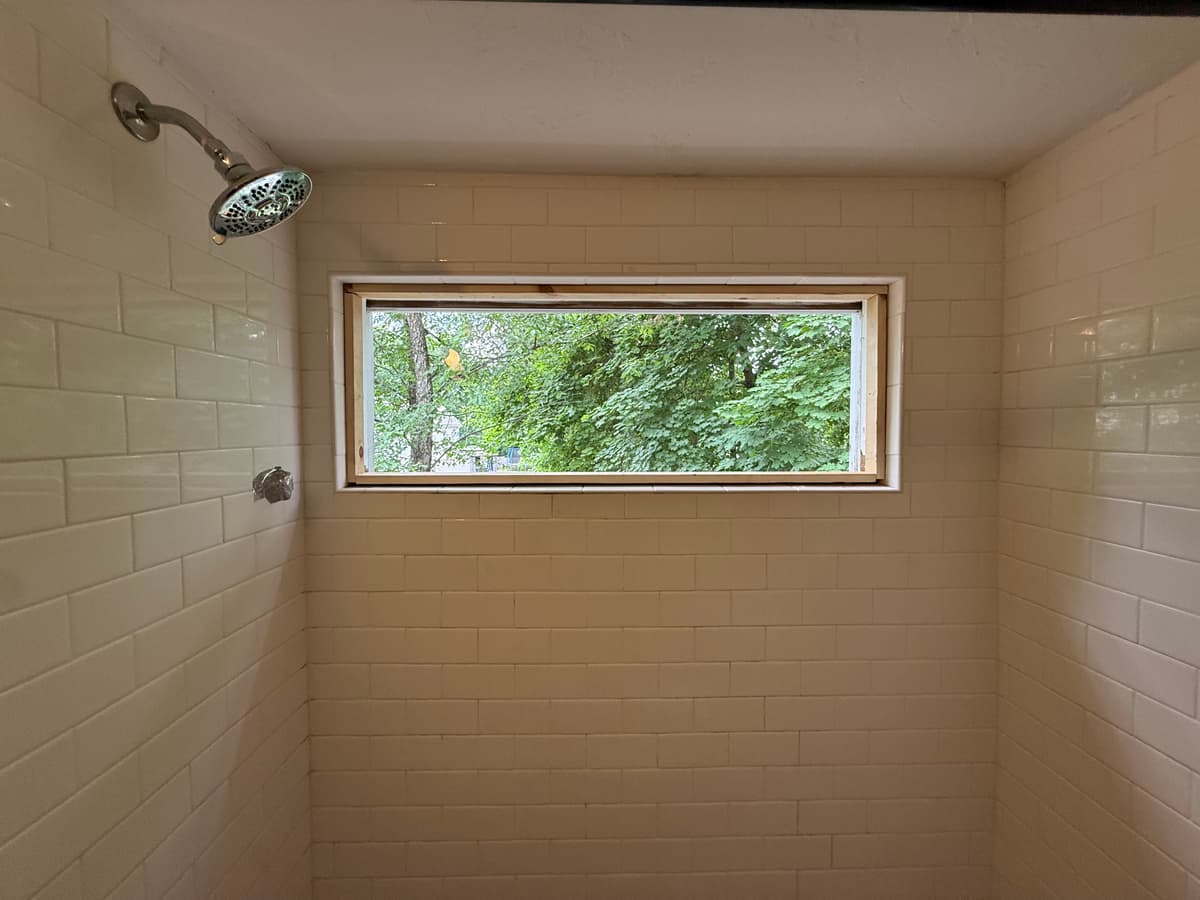 The opening sealed with a framed plexiglass panel, weather-tight until the tempered window arrives.